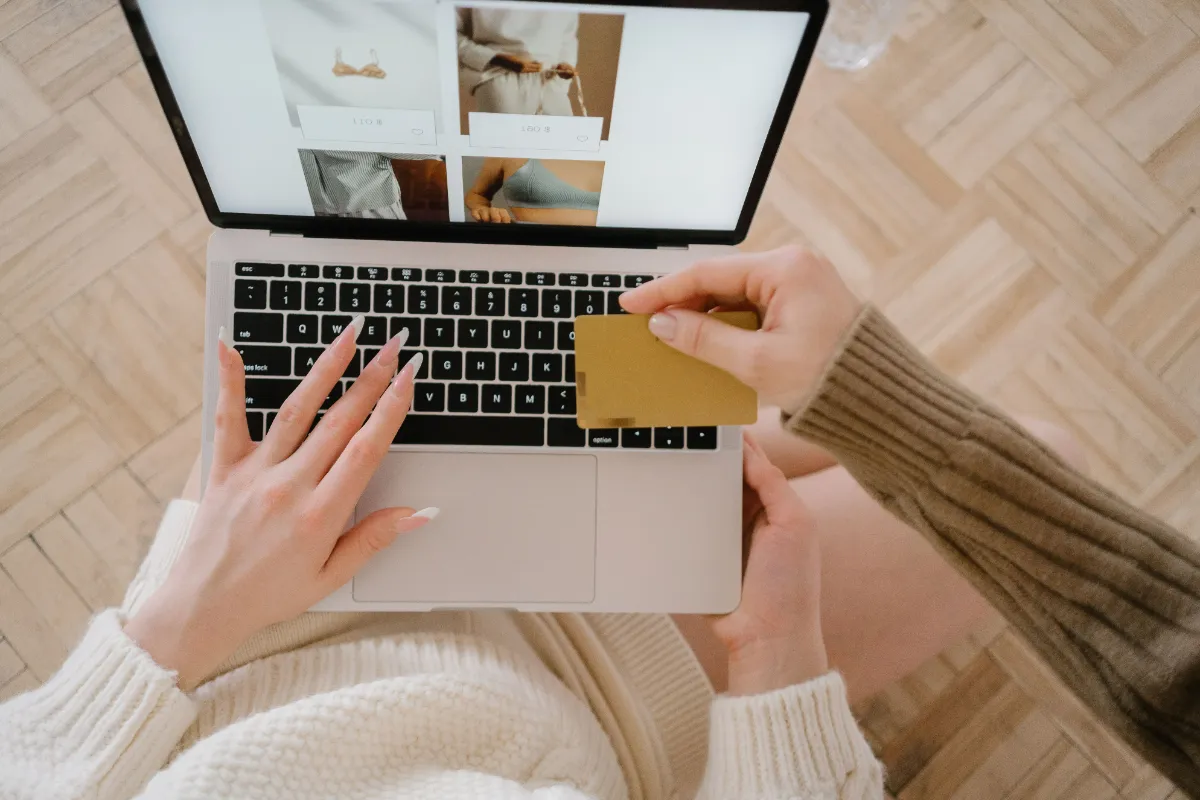 A shopper at a laptop holding a payment card while browsing an online store
